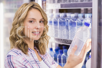 Portrait of a smiling pretty blonde woman taking a water bottle