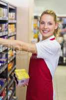 Portrait of a smiling blonde worker taking a product in shelf