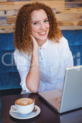 Pretty ginger having coffee using laptop