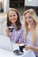 Two happy women friends looking at camera with cup of coffee