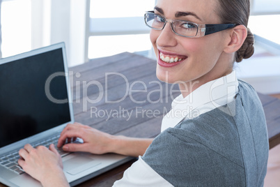 Businesswoman looking at camera with glasses and using laptop