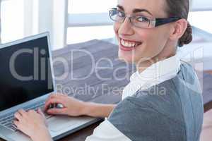 Businesswoman looking at camera with glasses and using laptop