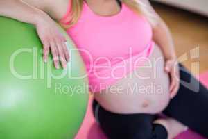 Pregnant woman touching her belly next to exercise ball
