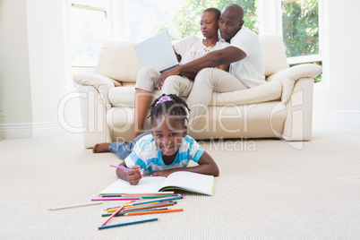 Pretty couple using laptop on couch and their daughter drawing