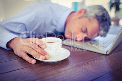 Businessman sleeping on laptop computer and touching coffee cup