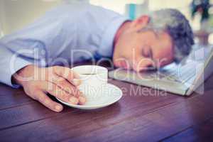 Businessman sleeping on laptop computer and touching coffee cup