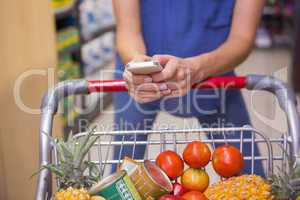 Woman pushing trolley in aisle and texting