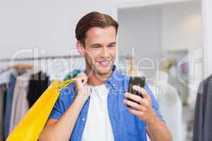A smiling man with shopping bags looking at his smartphone