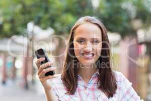 Pretty brunette smiling at camera and holding a smartphone