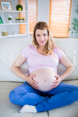 Pregnant woman looking at camera with hands on belly