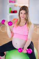 Pregnant woman lifting dumbbells on exercise ball