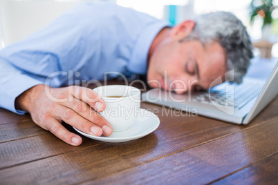 Businessman sleeping on laptop computer and touching coffee cup