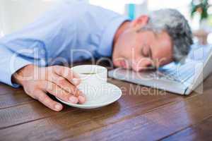 Businessman sleeping on laptop computer and touching coffee cup