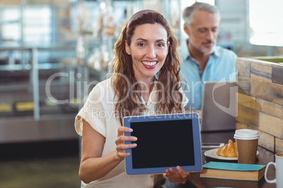 Pretty brunette looking at camera and showing tablet