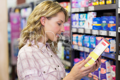 Side view of smiling pretty blonde woman looking at a product