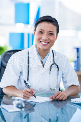 Happy doctor writing on a notebook and smiling at camera