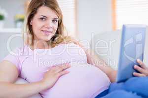 Pregnant woman looking at camera and using tablet