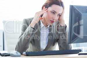 Upset business woman with head in hands in front of computer at