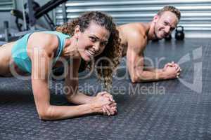Muscular couple doing planking exercises
