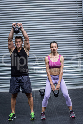 A muscular couple lifting kettlebells