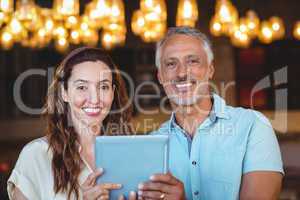 Happy couple smiling at camera and using tablet