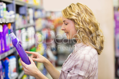 Side view of smiling pretty blonde woman looking at a product