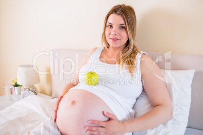 Pregnant woman lying on bed with apple in belly