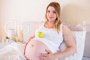 Pregnant woman lying on bed with apple in belly