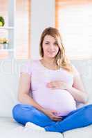 Pregnant woman looking at camera with hands on belly