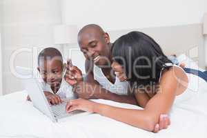 Pretty family using laptop together in bed