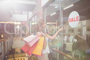 Smiling Woman with shopping bags pointing the window