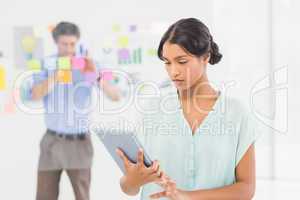 Creative businesswoman using tablet with colleague behind her