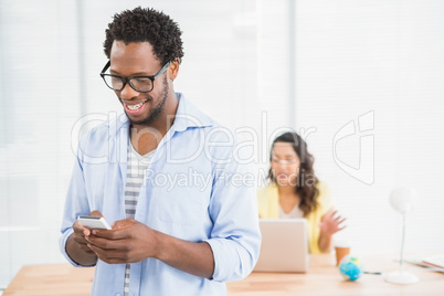 Smiling man posing in front of his colleague using smartphone