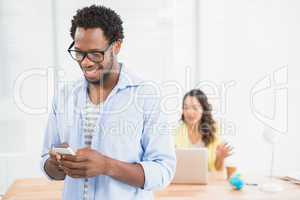 Smiling man posing in front of his colleague using smartphone