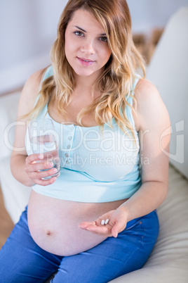 Pregnant woman looking at camera and taking a vitamin tablet