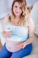 Pregnant woman looking at camera and taking a vitamin tablet