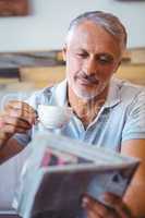 Smiling man having cup of coffee reading newspaper