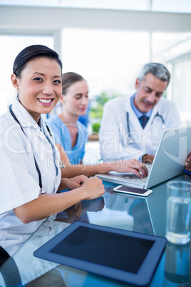 Happy doctor looking at camera while colleagues are talking