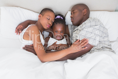 Pretty couple sleeping with their daughter in their bed