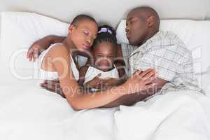 Pretty couple sleeping with their daughter in their bed