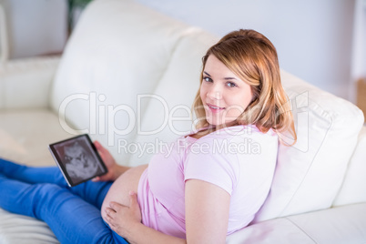 Pregnant woman looking at camera with hand on belly and ultrasou