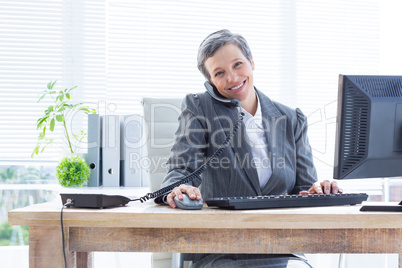 Smiling portrait businesswoman phoning and using computer