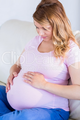 Pregnant woman sitting on couch touching her belly