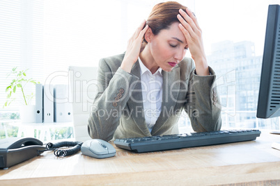 Upset business woman with head in hands in front of computer at