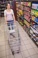 Pretty brunette pushing trolley and looking at shelf