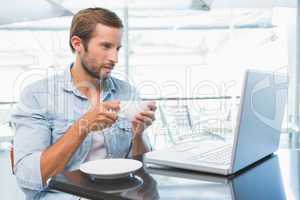 Young happy man holding his coffee while looking at his laptop