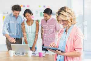 Casual businesswoman using digital tablet with colleagues behind