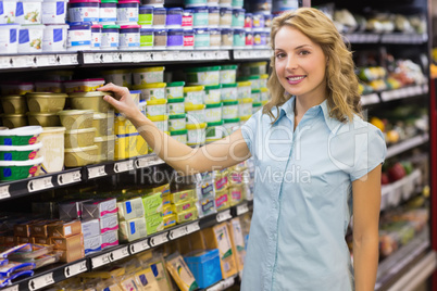 Portrait of smiling blonde woman taking a product in shelves