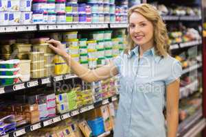 Portrait of smiling blonde woman taking a product in shelves