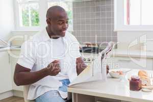 Smiling man reading a newspaper and drinking tea